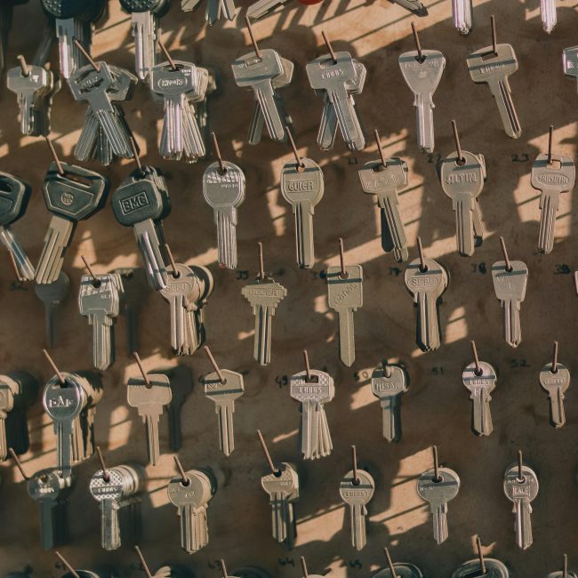 Une collection de clés métalliques variées suspendues à un mur avec des crochets, projetant des ombres.