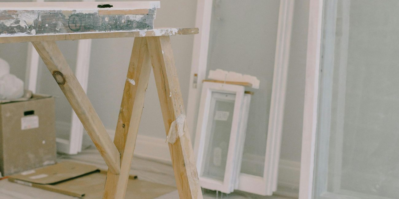 Intérieur d'une pièce avec un établi en bois et des fenêtres démontées des charnières, cadre blanc posé près du mur dans une pièce lumineuse pendant des travaux de rénovation