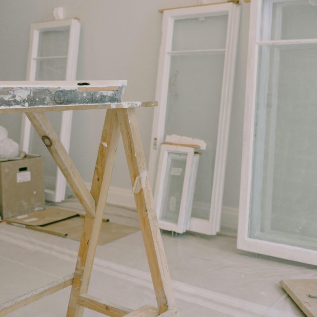 Intérieur d'une pièce avec un établi en bois et des fenêtres démontées des charnières, cadre blanc posé près du mur dans une pièce lumineuse pendant des travaux de rénovation