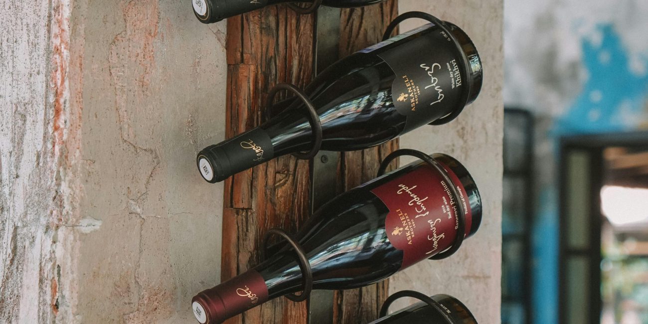 A rustic wooden rack elegantly displays various wine bottles against a textured wall. Un présentoir en bois rustique affiche élégamment diverses bouteilles de vin contre un mur texturé.