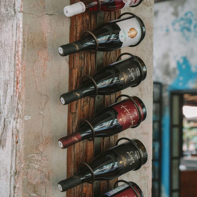 A rustic wooden rack elegantly displays various wine bottles against a textured wall. Un présentoir en bois rustique affiche élégamment diverses bouteilles de vin contre un mur texturé.