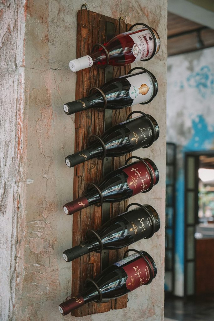 A rustic wooden rack elegantly displays various wine bottles against a textured wall. Un présentoir en bois rustique affiche élégamment diverses bouteilles de vin contre un mur texturé.