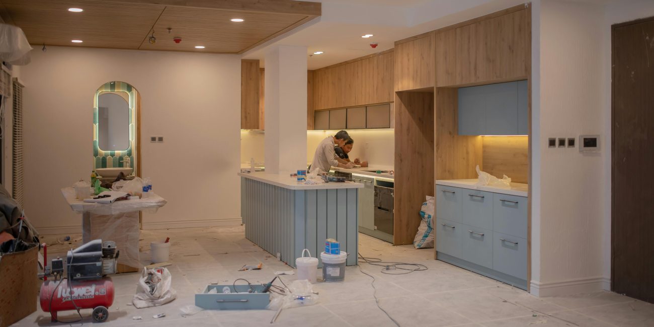 A modern kitchen undergoing renovation, featuring a worker, tools, and materials. Une cuisine moderne en cours de rénovation, mettant en vedette un ouvrier, des outils et des matériaux.
