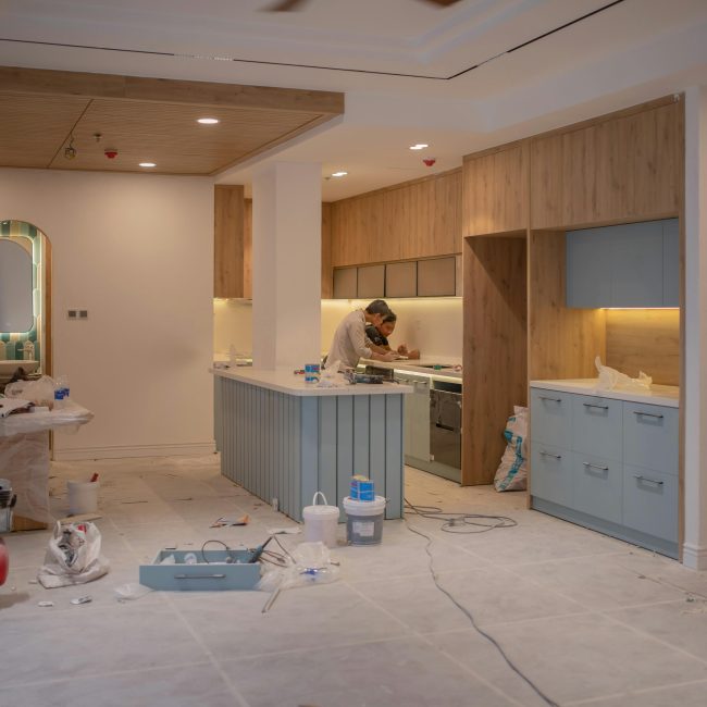 A modern kitchen undergoing renovation, featuring a worker, tools, and materials. Une cuisine moderne en cours de rénovation, mettant en vedette un ouvrier, des outils et des matériaux.