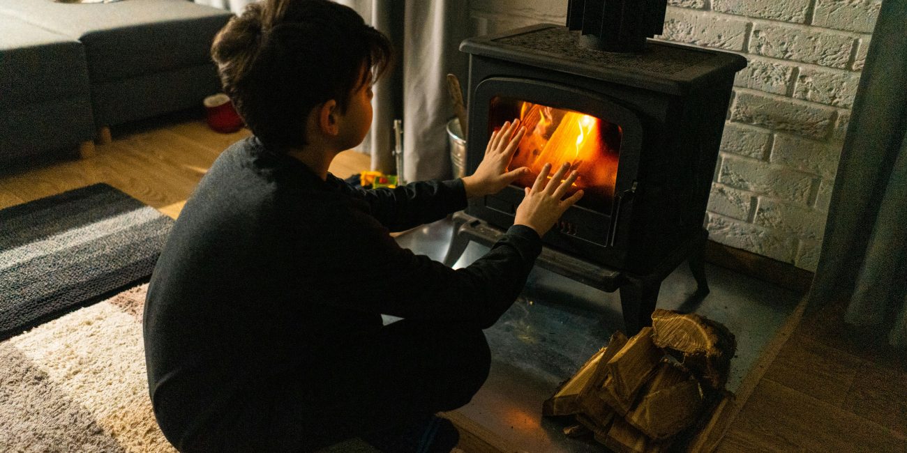 A child warms hands by a wood stove in a cozy living room, creating a warm winter ambiance. Un enfant se réchauffe les mains près d'un poêle à bois dans un salon douillet, créant une ambiance hivernale chaleureuse.