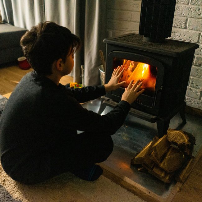 A child warms hands by a wood stove in a cozy living room, creating a warm winter ambiance. Un enfant se réchauffe les mains près d'un poêle à bois dans un salon douillet, créant une ambiance hivernale chaleureuse.