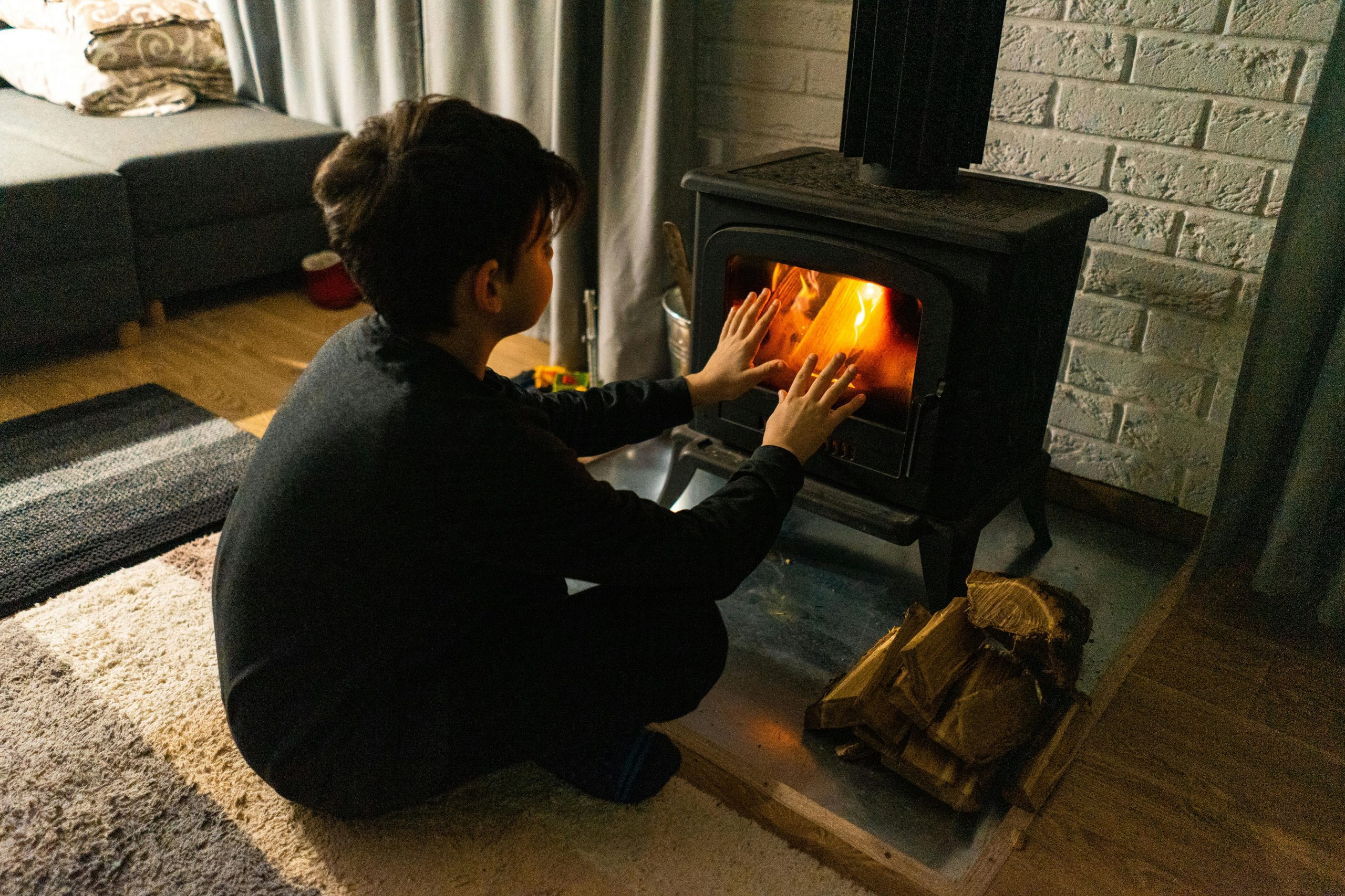 A child warms hands by a wood stove in a cozy living room, creating a warm winter ambiance. Un enfant se réchauffe les mains près d'un poêle à bois dans un salon douillet, créant une ambiance hivernale chaleureuse.