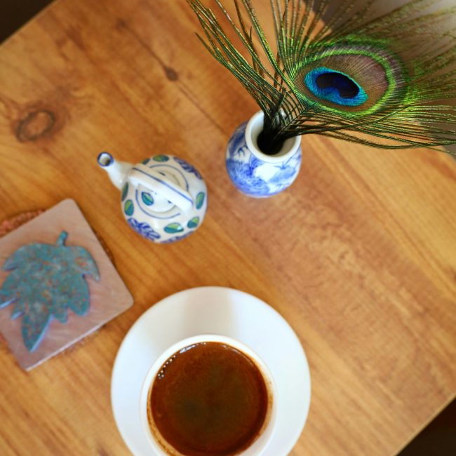 Top view of coffee cup, peacock feather, and ceramics on a table. Vue de dessus d'une tasse de café, d'une plume de paon et de céramiques sur une table.