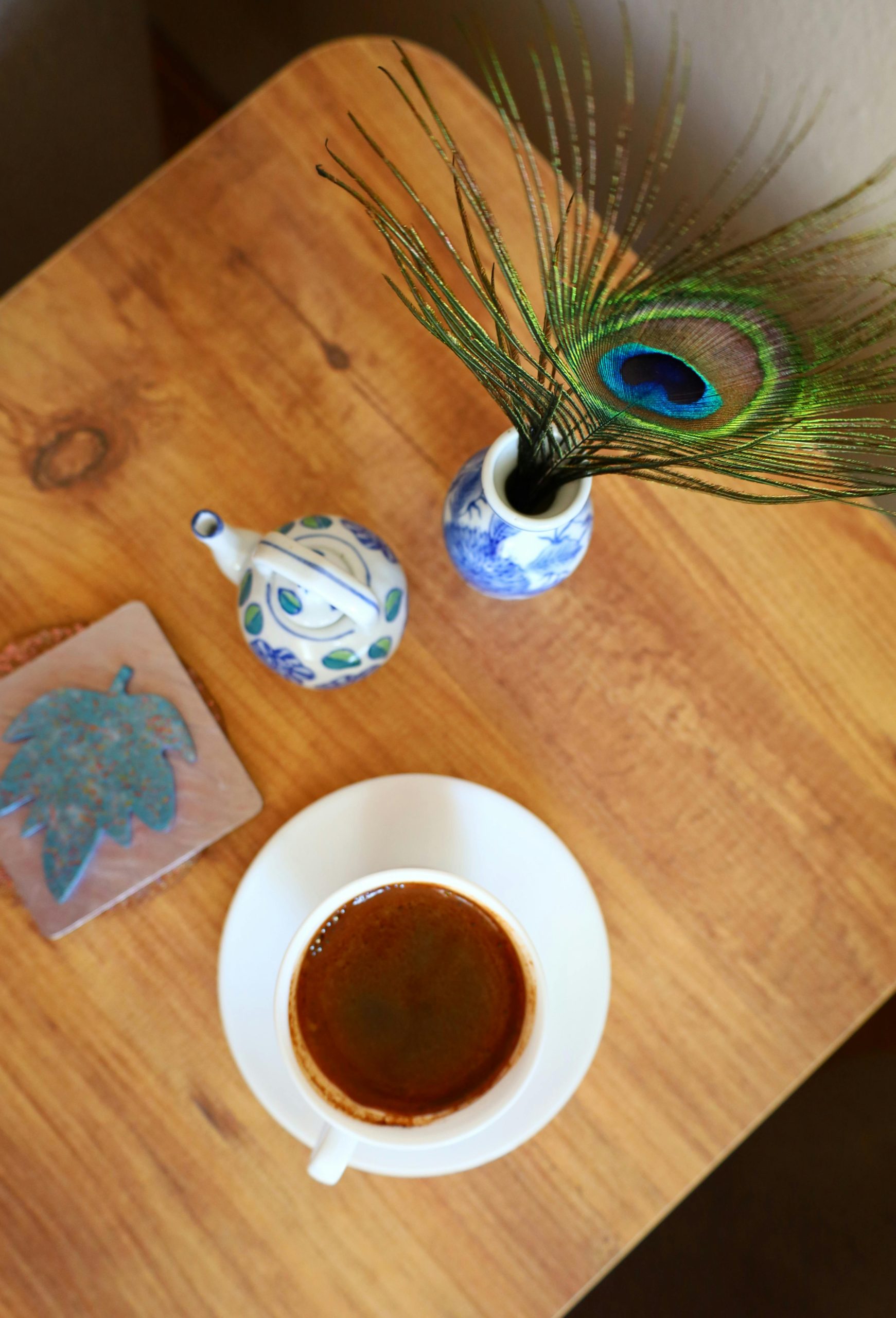 Top view of coffee cup, peacock feather, and ceramics on a table. Vue de dessus d'une tasse de café, d'une plume de paon et de céramiques sur une table.