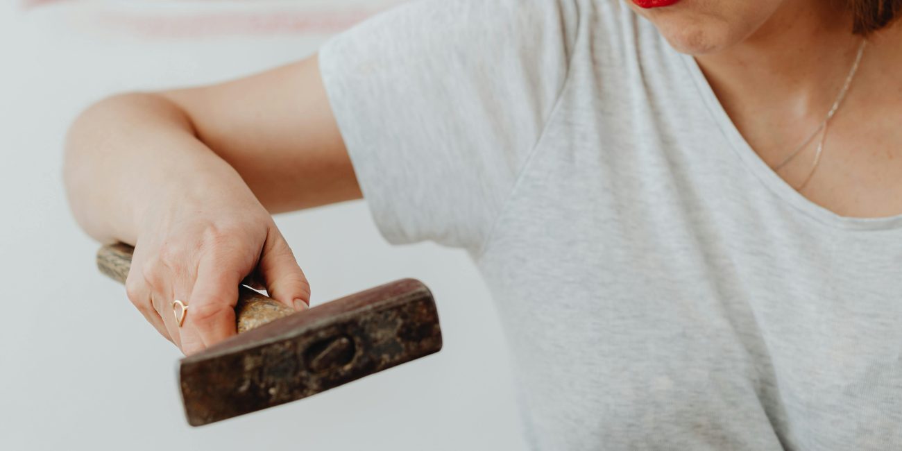 A woman struggling with a DIY project, exhibiting frustration with a hammer and nail. Une femme en difficulté avec un projet de bricolage, montrant de la frustration avec un marteau et un clou.