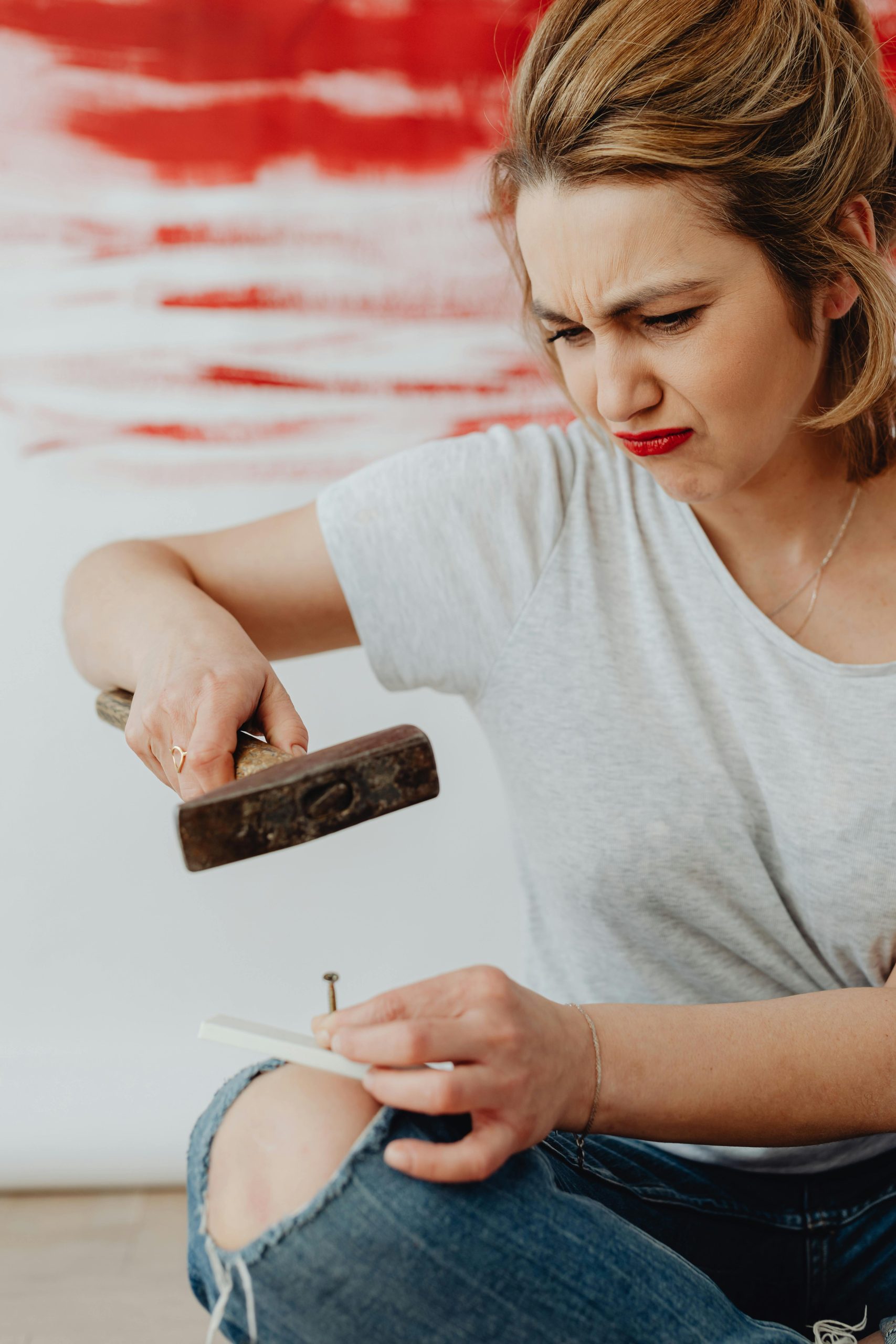 A woman struggling with a DIY project, exhibiting frustration with a hammer and nail. Une femme en difficulté avec un projet de bricolage, montrant de la frustration avec un marteau et un clou.