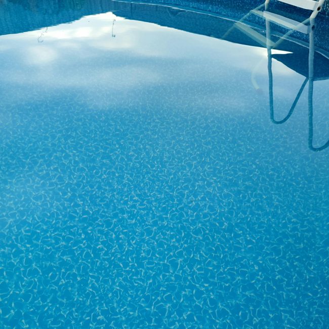 Captivating view of a blue swimming pool with a ladder reflected on the surface, ideal summer relaxation spot. Vue captivante d'une piscine bleue avec une échelle reflétée à la surface, un endroit idéal pour la détente estivale.