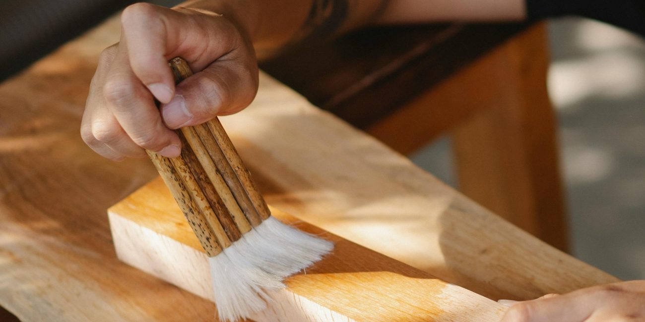 High angle of unrecognizable artisan using brush for varnishing wooden beam while working in professional workshop Vue de haut d'un artisan non identifiable utilisant un pinceau pour vernir une poutre en bois tout en travaillant dans un atelier professionnel