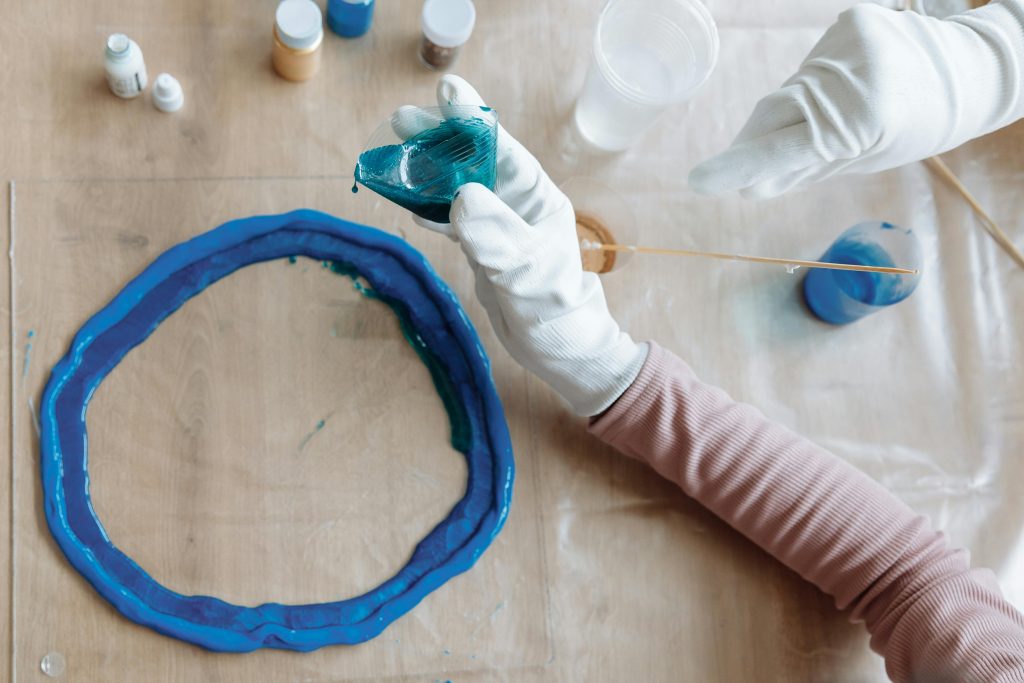 Close-up of hands crafting blue resin art indoors, showcasing artistic process. Gros plan sur des mains créant de l'art en résine bleue en intérieur, montrant le processus artistique.