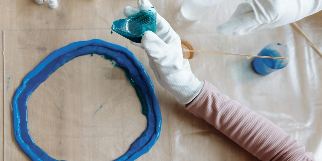 Close-up of hands crafting blue resin art indoors, showcasing artistic process. Gros plan sur des mains créant de l'art en résine bleue en intérieur, montrant le processus artistique.