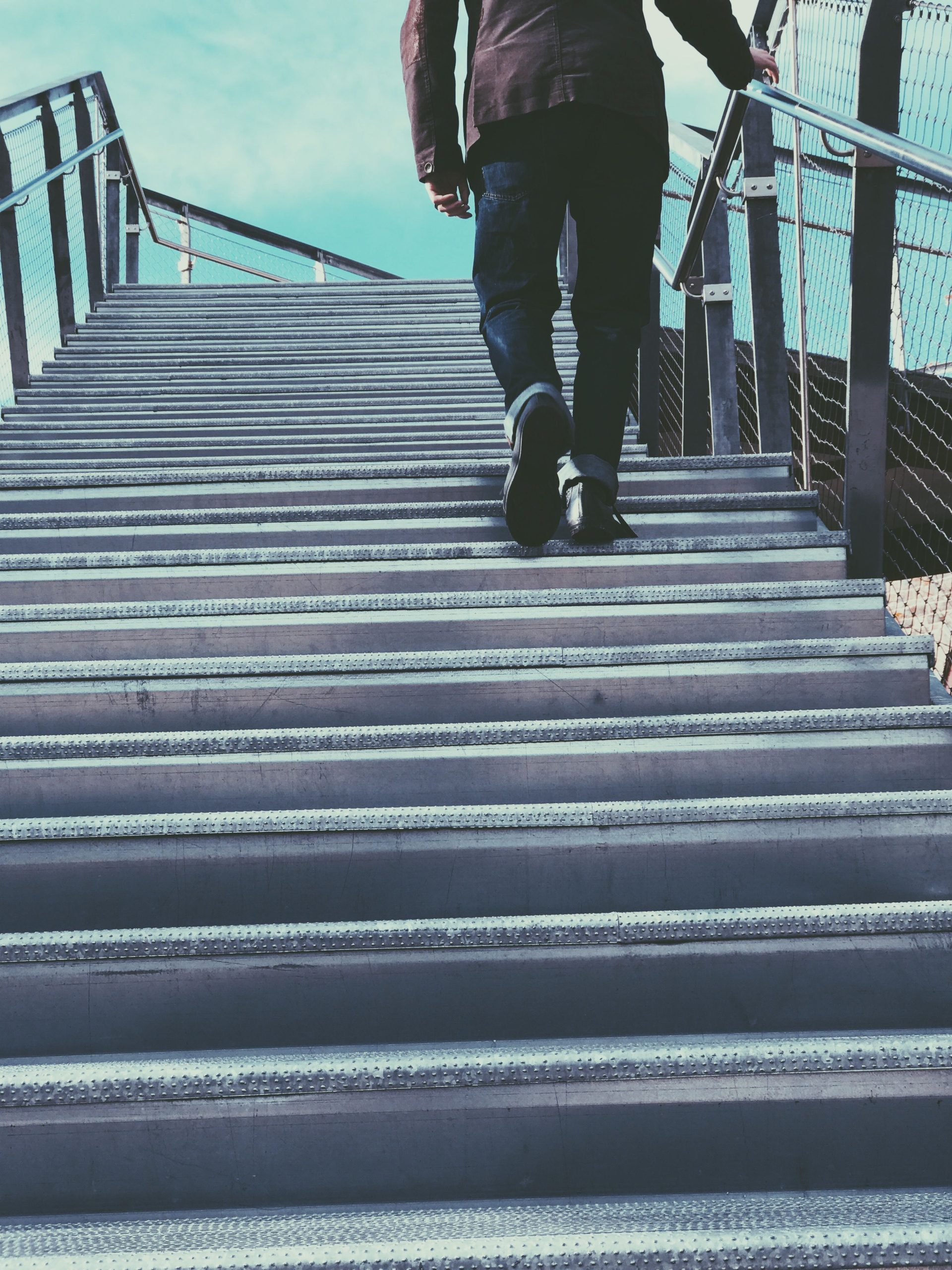 A person in casual wear ascends a metal staircase in an urban setting, suggesting travel or progress. Une personne en tenue décontractée monte un escalier métallique dans un cadre urbain, suggérant un voyage ou une progression.
