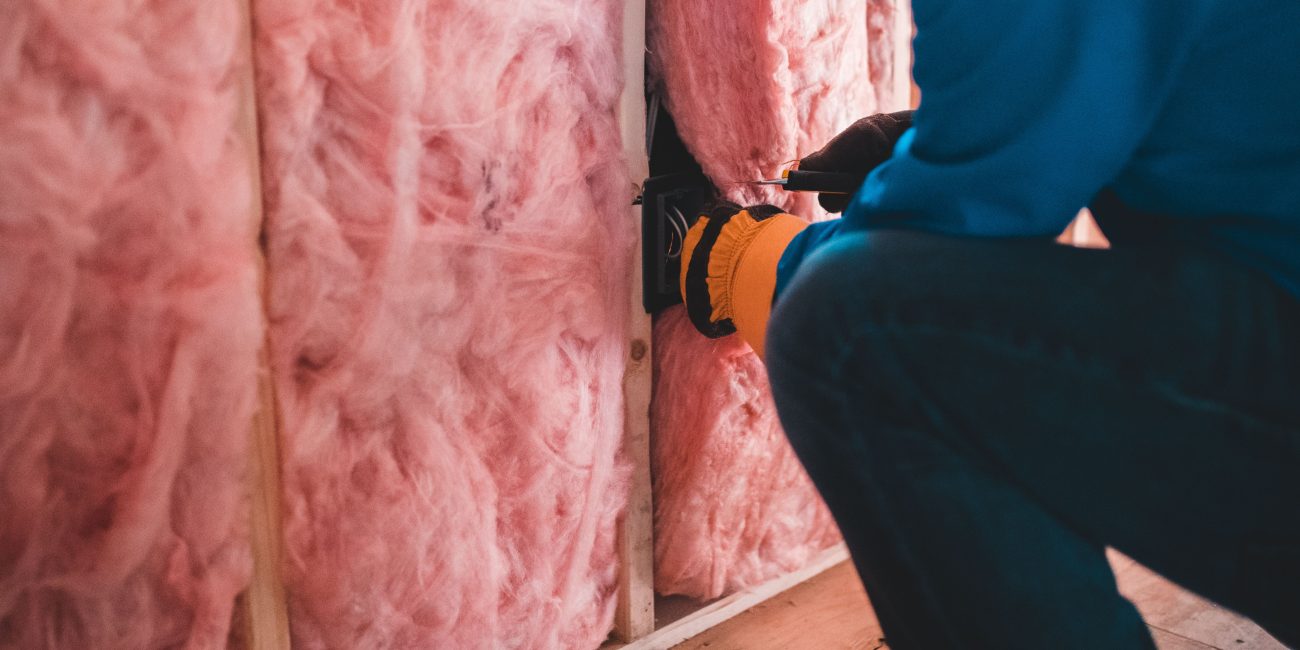 Crop unrecognizable worker in gloves sitting on haunches and insulating with pink stone wool Ouvrier méconnaissable en gants accroupi et isolant avec de la laine de pierre rose