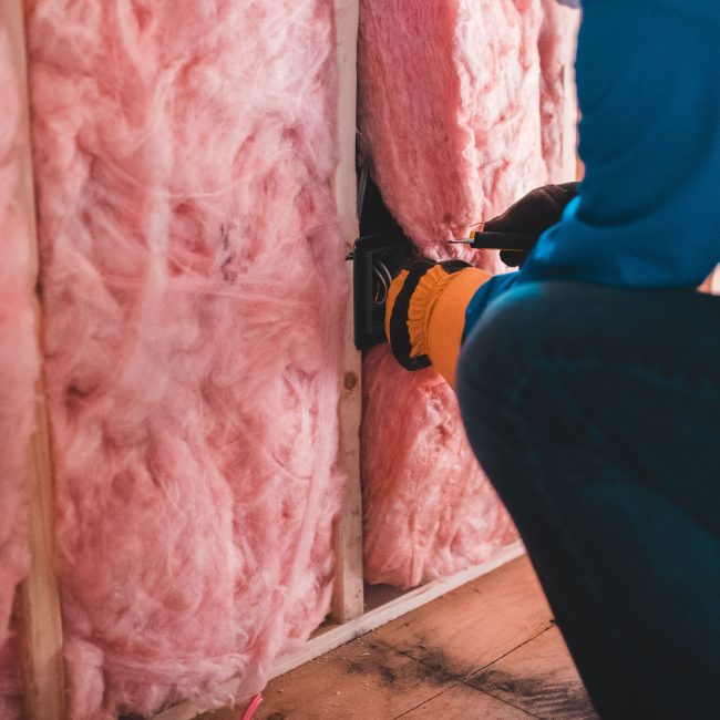 Crop unrecognizable worker in gloves sitting on haunches and insulating with pink stone wool Ouvrier méconnaissable en gants accroupi et isolant avec de la laine de pierre rose