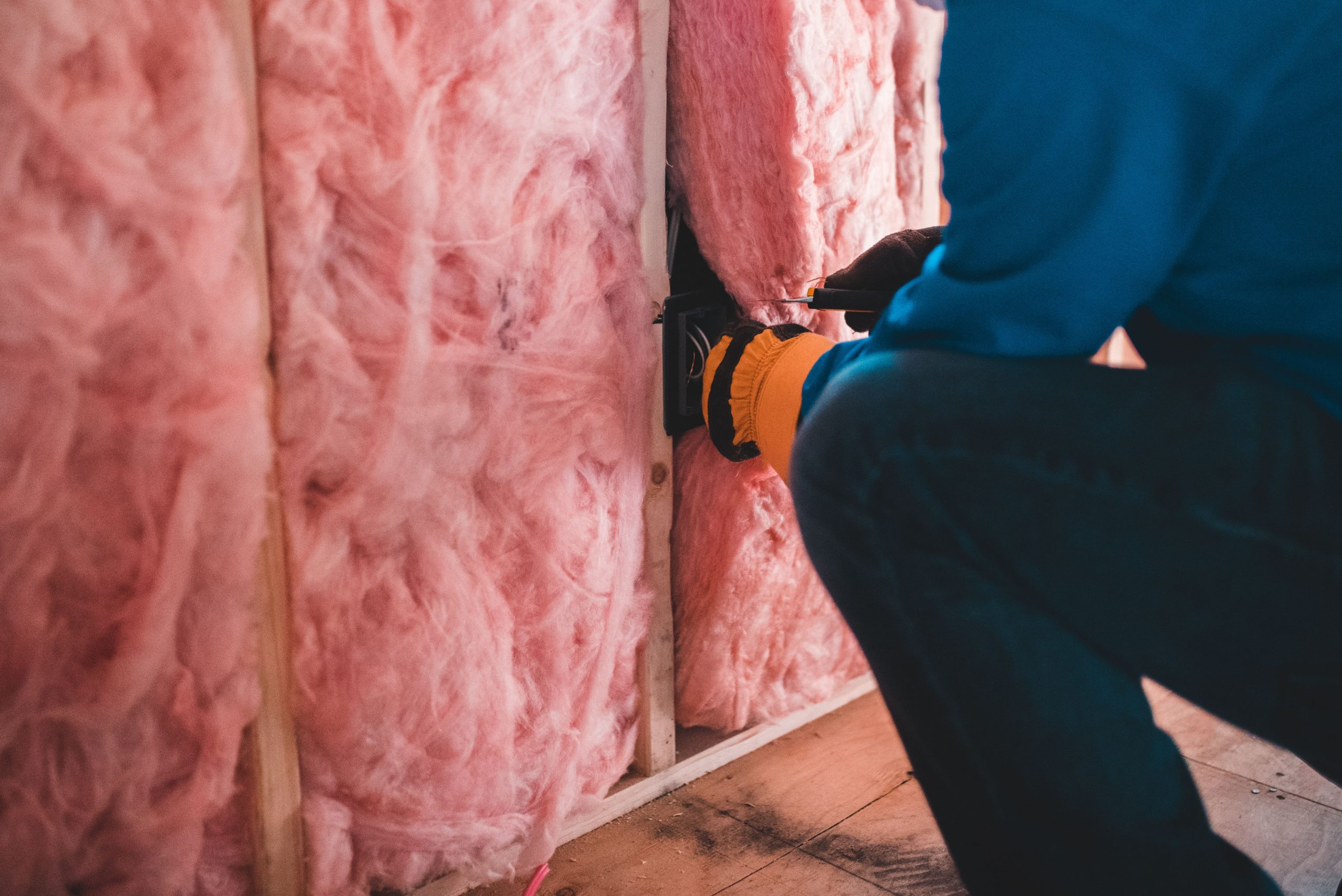 Travailleur méconnaissable accroupi avec des gants isolant avec de la laine de pierre rose