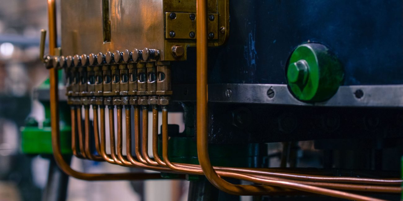 Detailed view of industrial machinery featuring copper tubing and steel components in a factory setting. Vue détaillée de machines industrielles présentant des tubes en cuivre et des composants en acier dans un environnement d'usine.