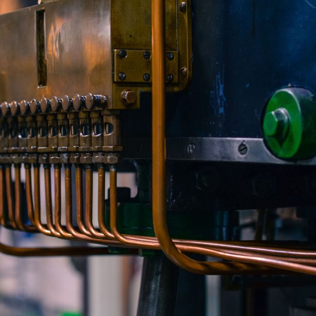 Detailed view of industrial machinery featuring copper tubing and steel components in a factory setting. Vue détaillée de machines industrielles présentant des tubes en cuivre et des composants en acier dans un environnement d'usine.