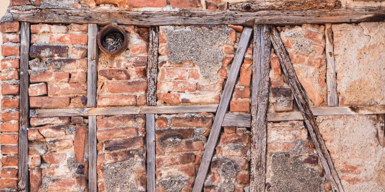 Close-up of an old brick wall showing decay and exposed wooden beams. Gros plan d'un vieux mur de briques montrant une détérioration et des poutres en bois exposées.