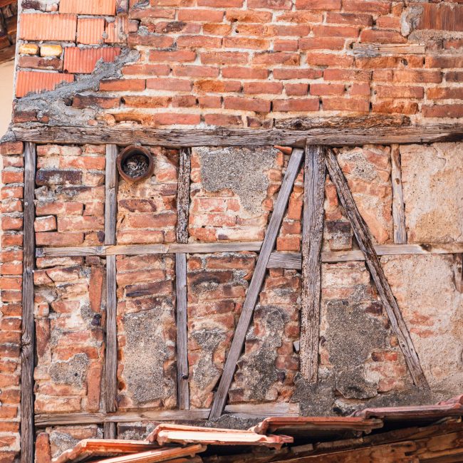 Close-up of an old brick wall showing decay and exposed wooden beams. Gros plan d'un vieux mur de briques montrant une détérioration et des poutres en bois exposées.