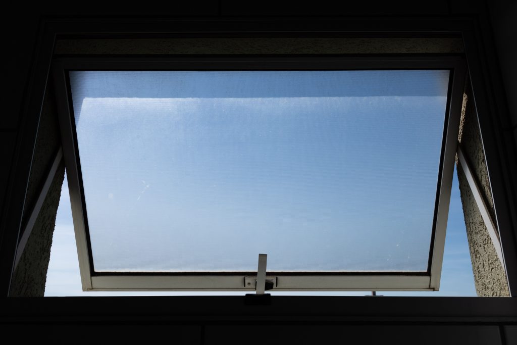 A low angle view of an open skylight window revealing a clear blue sky. Vue en plongée d'une lucarne ouverte révélant un ciel bleu dégagé.