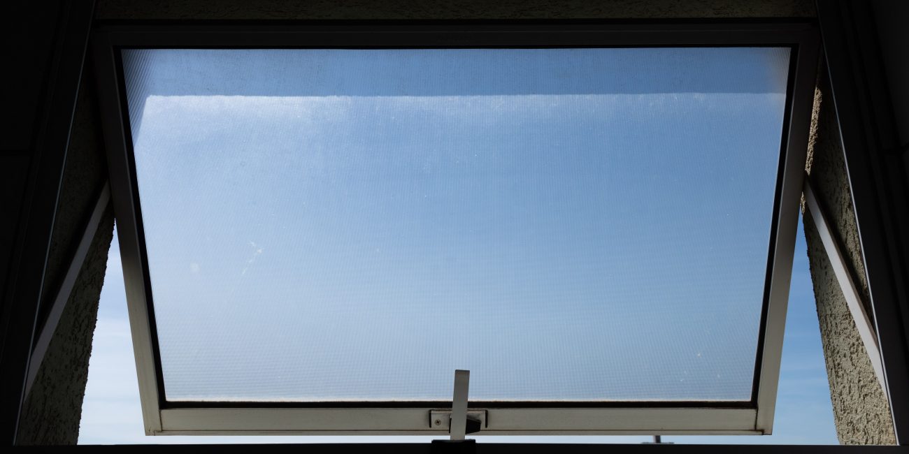 A low angle view of an open skylight window revealing a clear blue sky. Vue en plongée d'une lucarne ouverte révélant un ciel bleu dégagé.