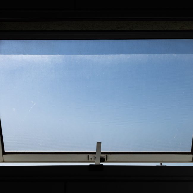 A low angle view of an open skylight window revealing a clear blue sky. Vue en plongée d'une lucarne ouverte révélant un ciel bleu dégagé.