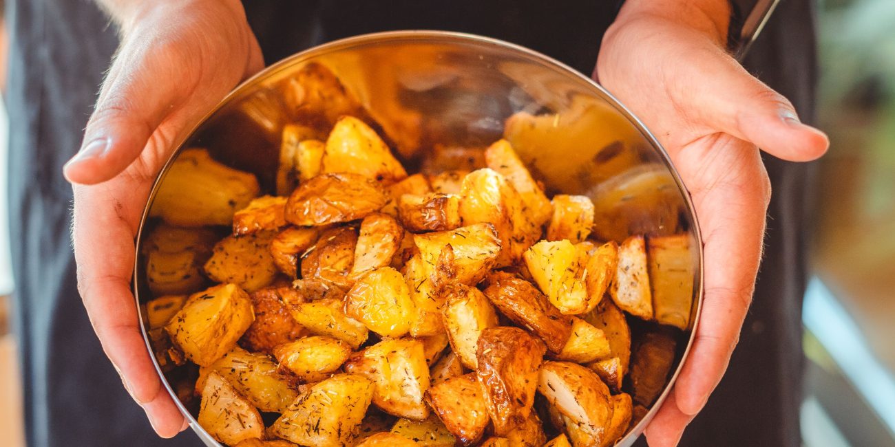 From above of crop unrecognizable person in apron holding plate with pieces of delicious fried potato Vue de dessus d'une personne méconnaissable en tablier tenant une assiette avec des morceaux de délicieuses pommes de terre frites.