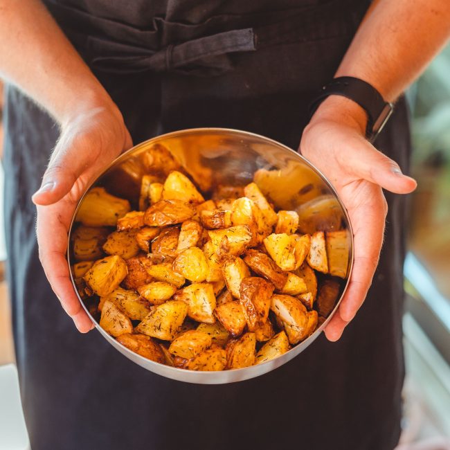 From above of crop unrecognizable person in apron holding plate with pieces of delicious fried potato Vue de dessus d'une personne méconnaissable en tablier tenant une assiette avec des morceaux de délicieuses pommes de terre frites.