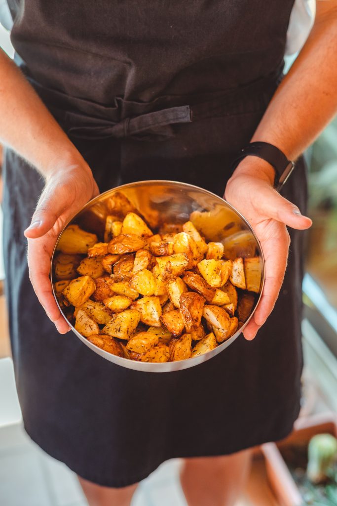 From above of crop unrecognizable person in apron holding plate with pieces of delicious fried potato Vue de dessus d'une personne méconnaissable en tablier tenant une assiette avec des morceaux de délicieuses pommes de terre frites.