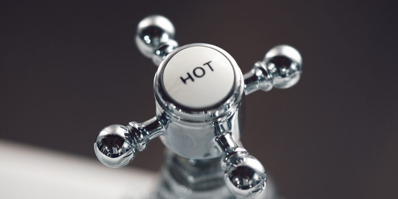 Elegant vintage chrome faucet handle labeled 'Hot' with blurred background. Poignée de robinet chromée vintage élégante étiquetée « Hot » avec arrière-plan flou.