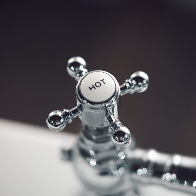 Elegant vintage chrome faucet handle labeled 'Hot' with blurred background. Poignée de robinet chromée vintage élégante étiquetée « Hot » avec arrière-plan flou.