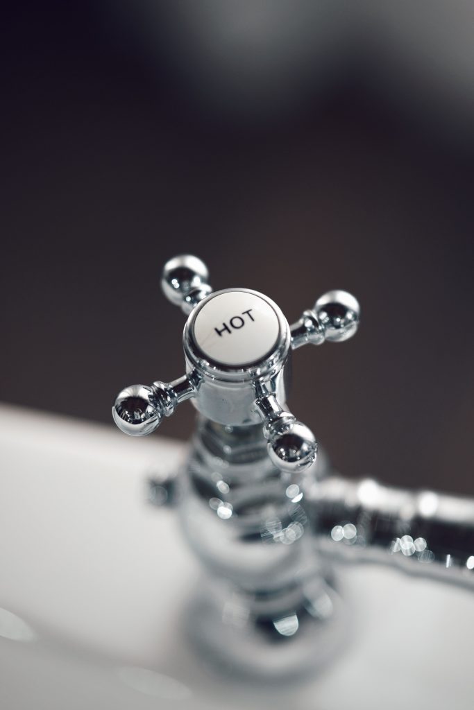 Elegant vintage chrome faucet handle labeled 'Hot' with blurred background. Poignée de robinet chromée vintage élégante étiquetée « Hot » avec arrière-plan flou.
