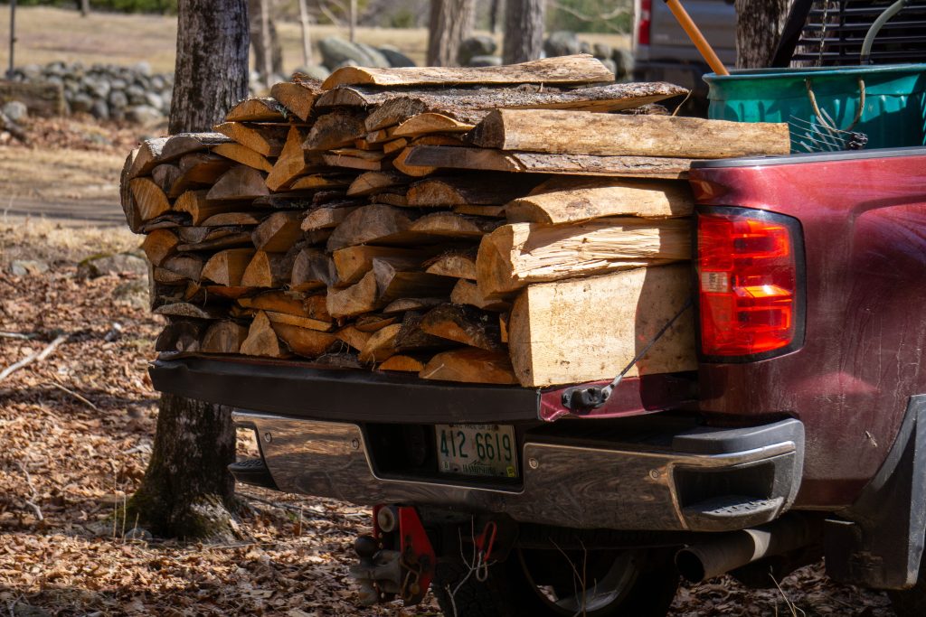 A pickup truck carrying a full load of split firewood in the forest, ready for transport. Un camion pickup transportant un chargement complet de bois de chauffage fendu en forêt, prêt pour le transport.