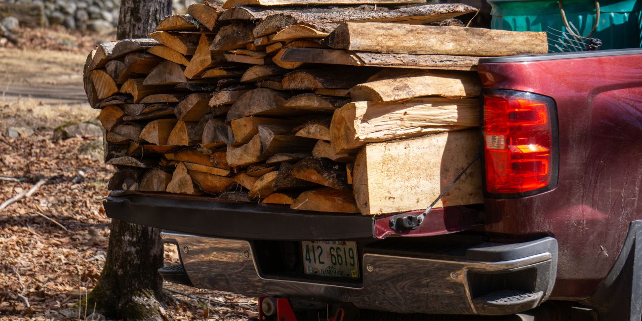 A pickup truck carrying a full load of split firewood in the forest, ready for transport. Un camion pickup transportant un chargement complet de bois de chauffage fendu en forêt, prêt pour le transport.
