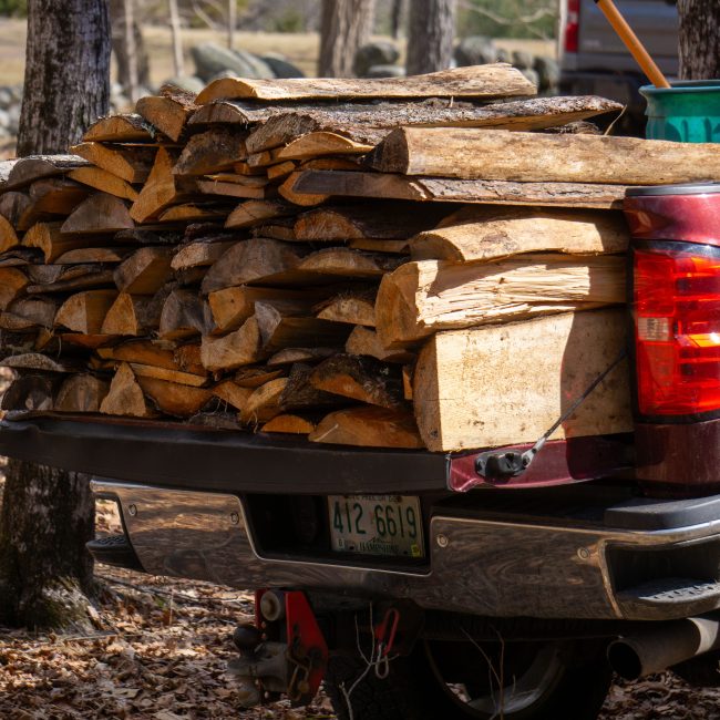 A pickup truck carrying a full load of split firewood in the forest, ready for transport. Un camion pickup transportant un chargement complet de bois de chauffage fendu en forêt, prêt pour le transport.