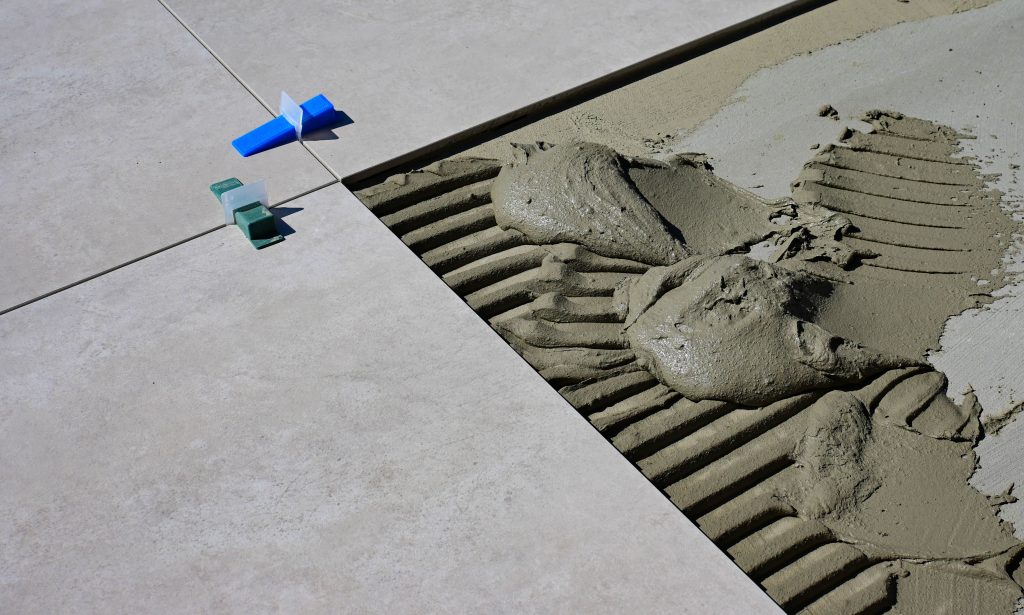 Close-up of wet cement and tile spacers during floor tile installation. Gros plan sur du ciment mouillé et des entretoises de carrelage lors de l'installation de carrelage de sol.