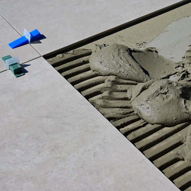 Close-up of wet cement and tile spacers during floor tile installation. Gros plan sur du ciment mouillé et des entretoises de carrelage lors de l'installation de carrelage de sol.